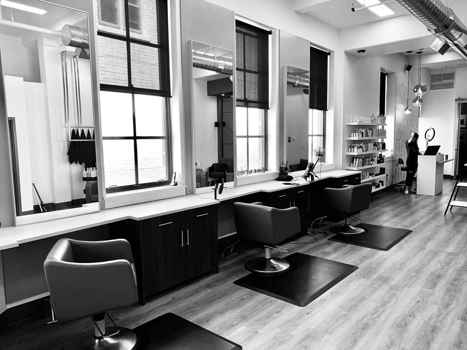 Schwarzweißfoto einer Frau mit Laptop neben drei Salonstühlen